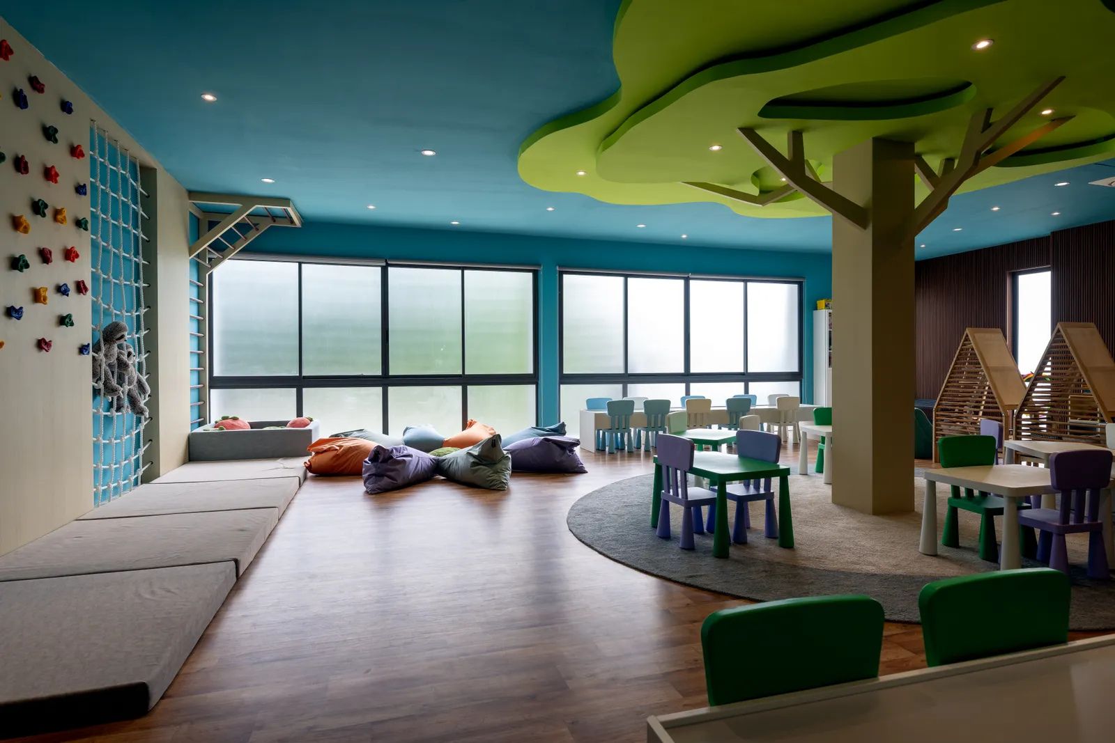 The Kokko Learning Studio: a bright room with coloured tables, beanbags, a climbing wall and a tree in the middle.