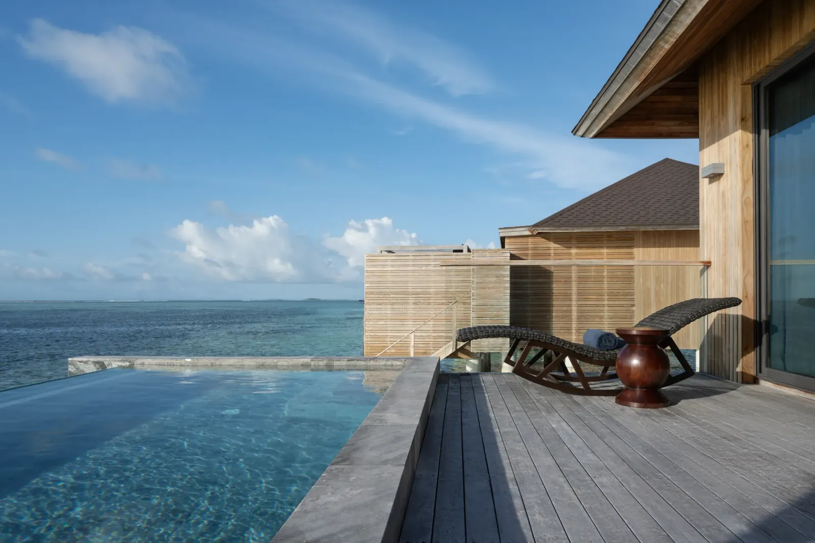An Aqua Pool Villa’s deck over the water: the infinity pool, the timber lounger and the ocean to the horizon.