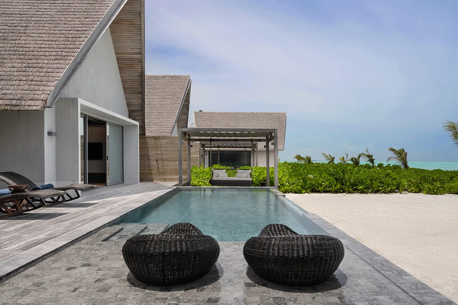 A Serene Pool Villa on the beach: the long pool in front of the white-roofed villa, the pergola and the lawn.