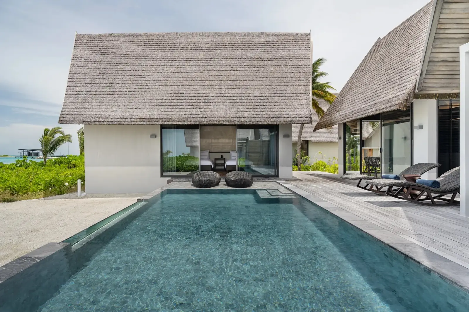The Two-Bedroom Serene Pool Villa: the long pool between its 2 thatched wings and the loungers on the deck.