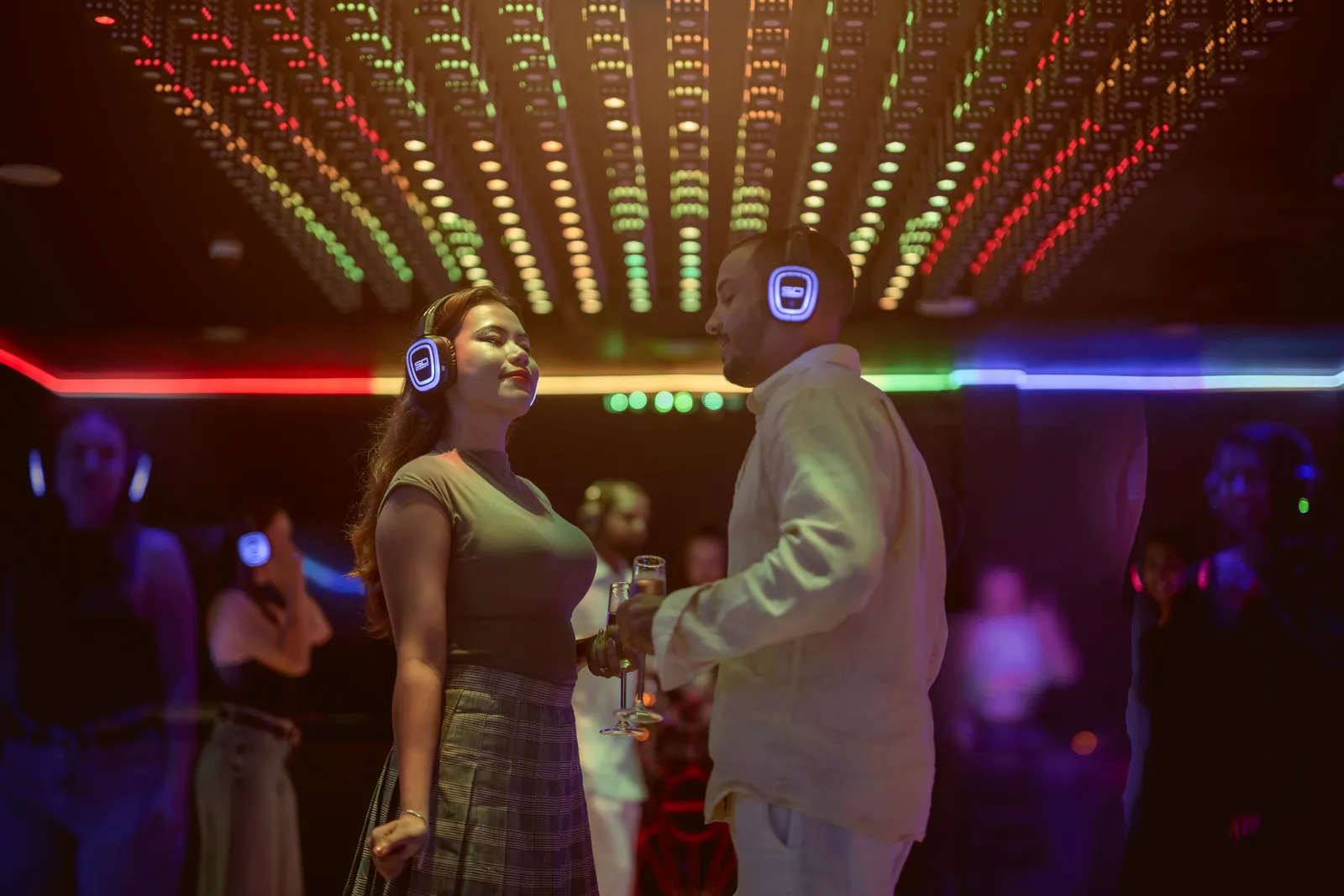 The Silent DJ room: 2 guests dancing in glowing headphones under a ceiling of coloured lights.