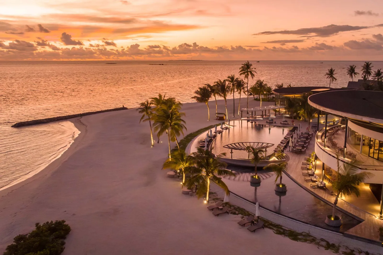 The main pool and the beach at sunset, seen from above, with the lights on among the palms.