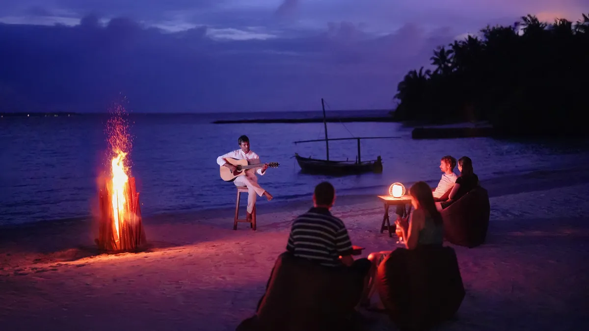 The evening bonfire on the beach, a guitarist playing and guests sitting round it.