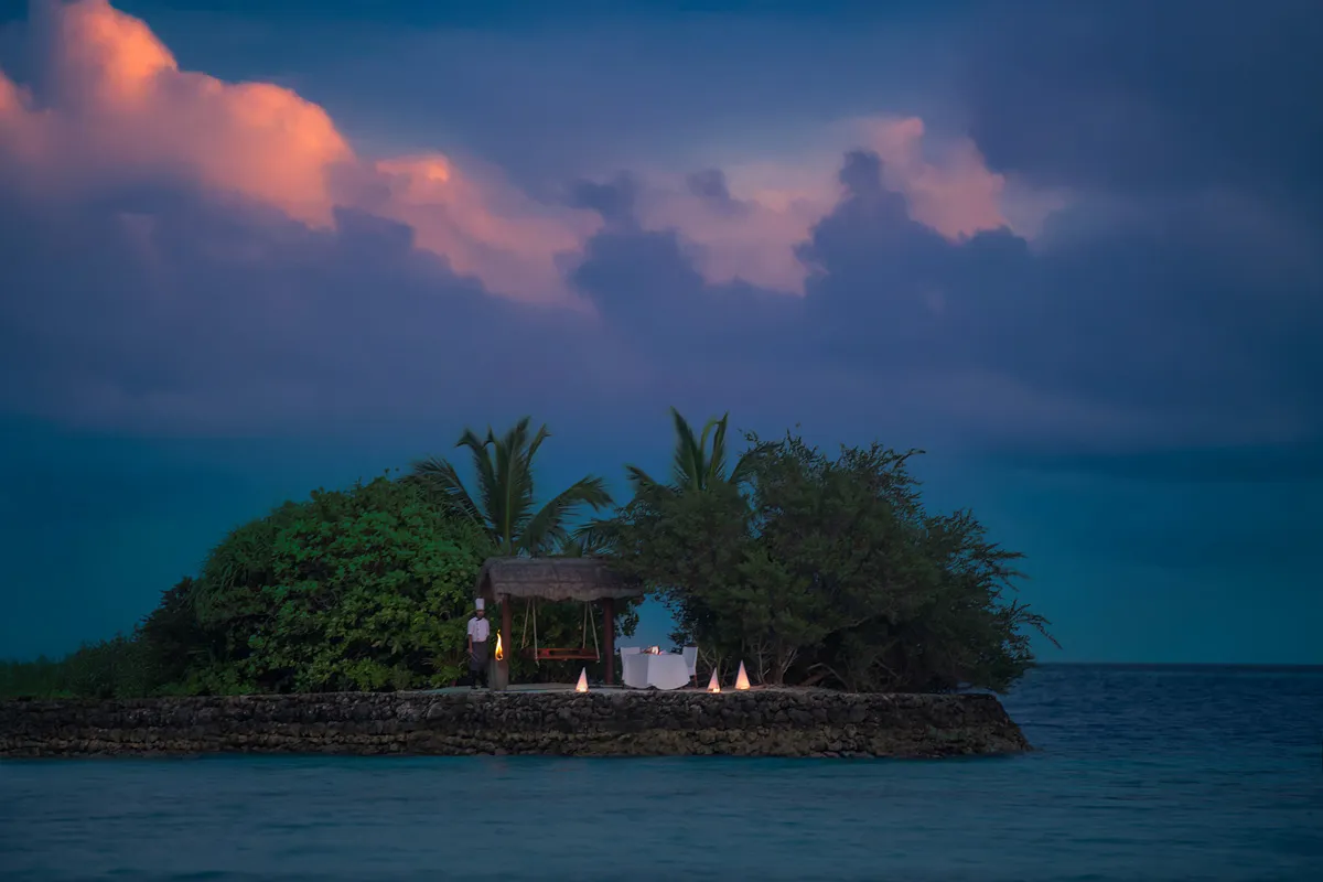 Rock Island at dusk, the islet reached by a short bridge, torches lit for a private dinner.