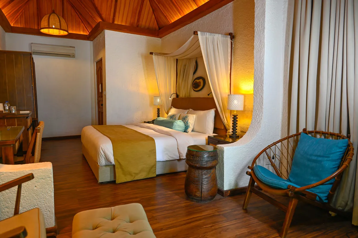 A Beach Bungalow bedroom, with its double bed, the rocking chair and the curtain onto the bathroom.