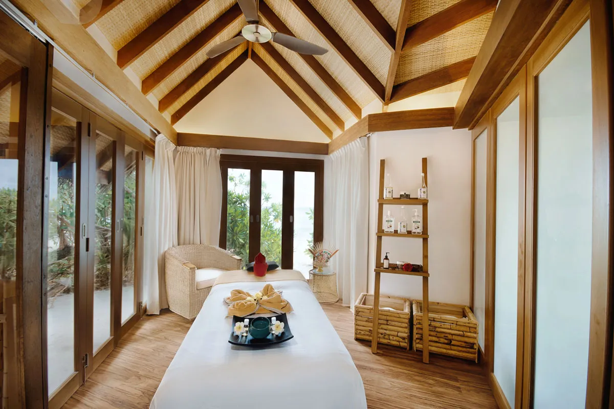 An Aavun Spa treatment room, its massage bed, glass doors onto the garden and a timber ceiling.
