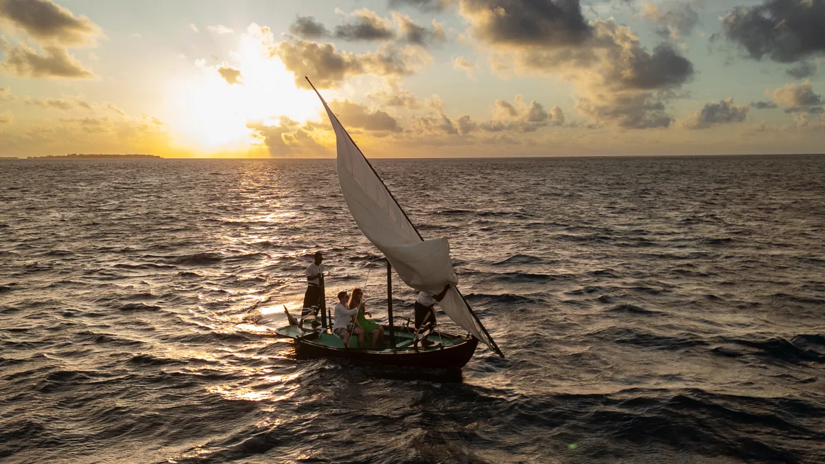 The resort’s sailing dhoni at sunset, a couple aboard on a calm sea.