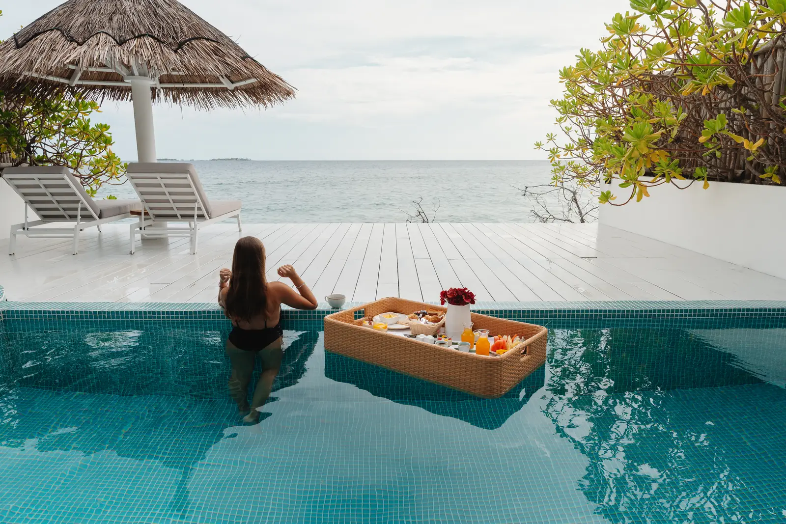 A floating breakfast in a private pool: the wicker tray on the water, a guest at the edge and the sea ahead.