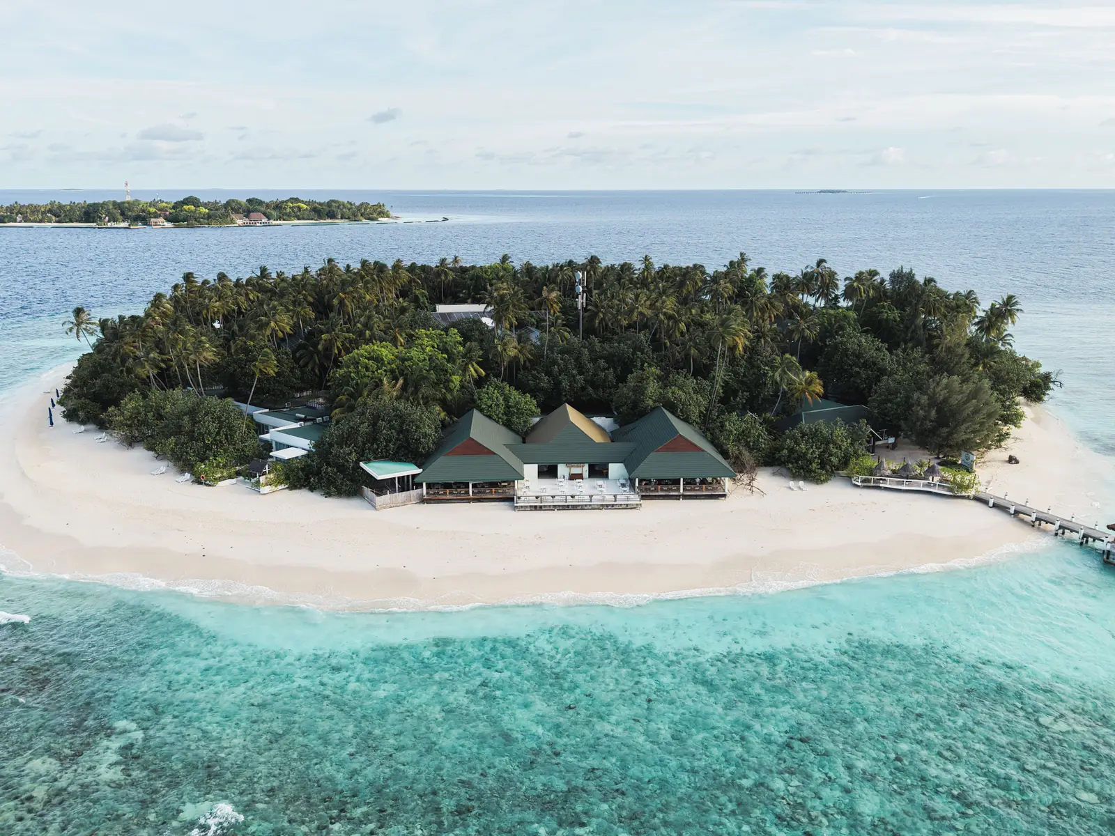 Kuda Bandos from the air: the white beach, the green roofs on the shore, the jetty and another island of the atoll beyond.