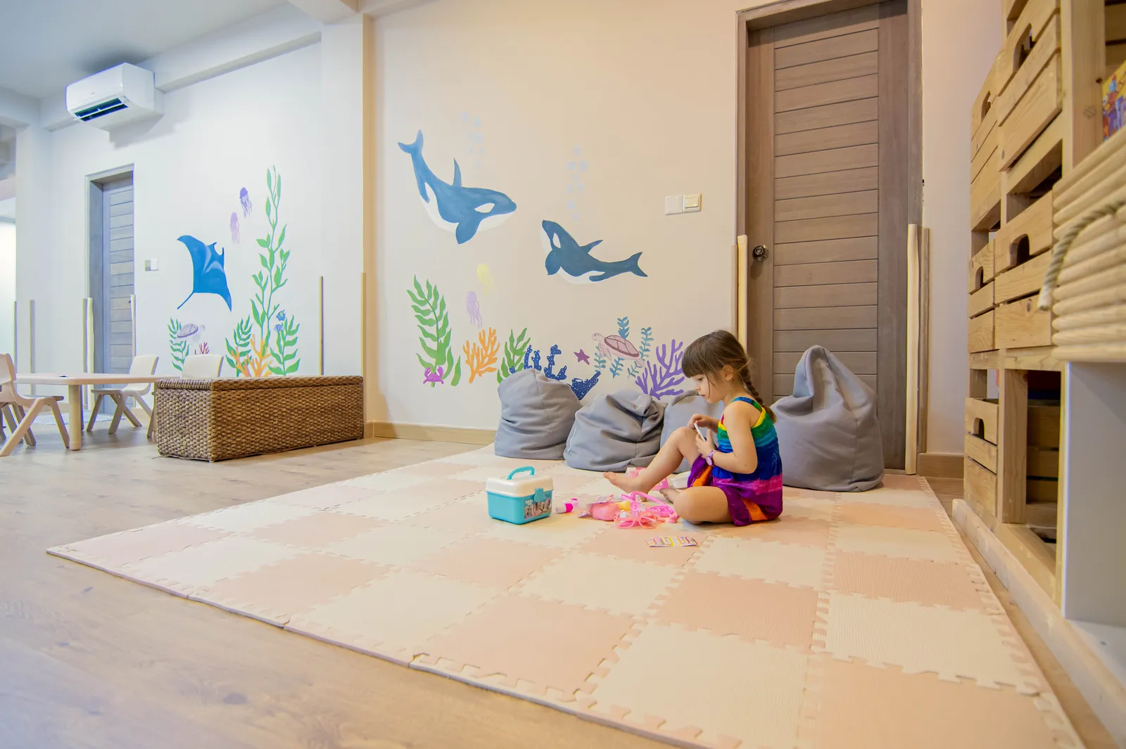 A girl plays on the mat of the Koyya Kids Club, among beanbags and orcas painted on the wall.