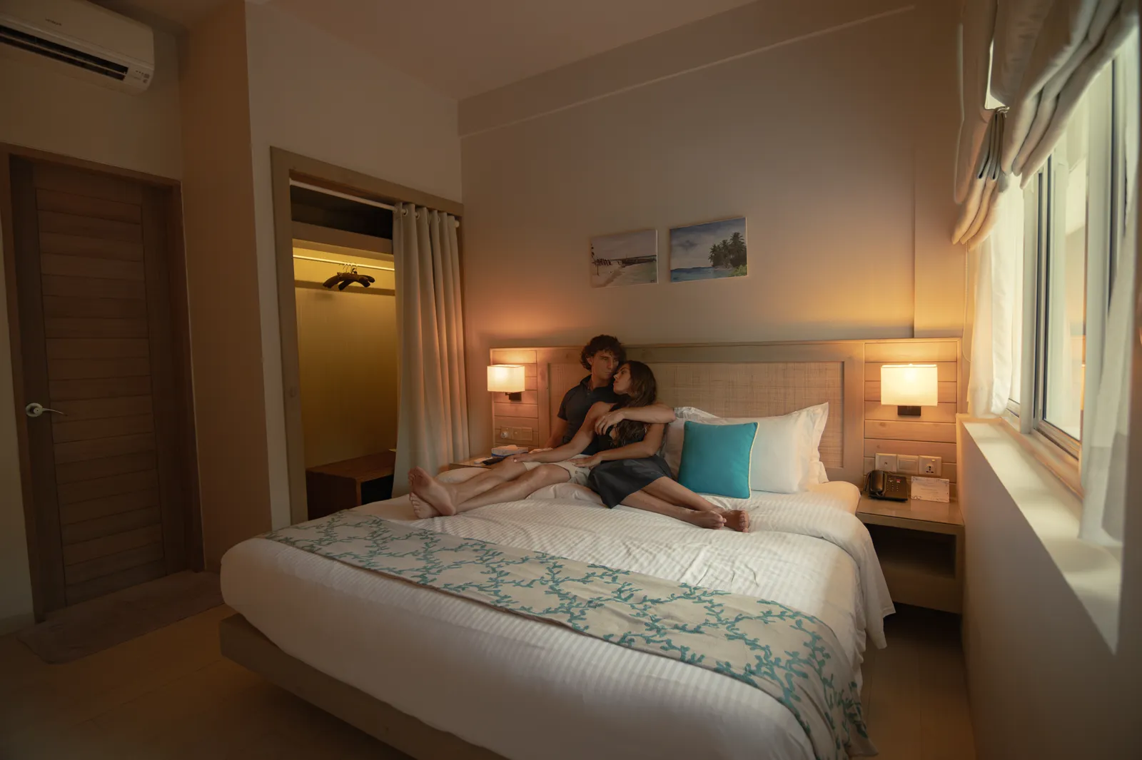 A Superior Room in the evening: a couple on the bed, the lamps on and the window with its Roman blind.