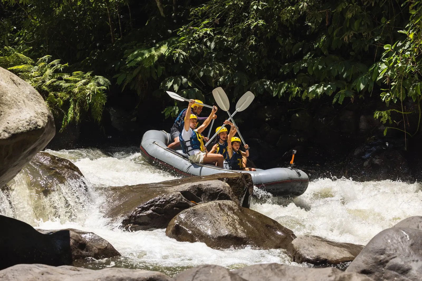 A raft in the Ayung’s rapids, boulders and green banks around it
