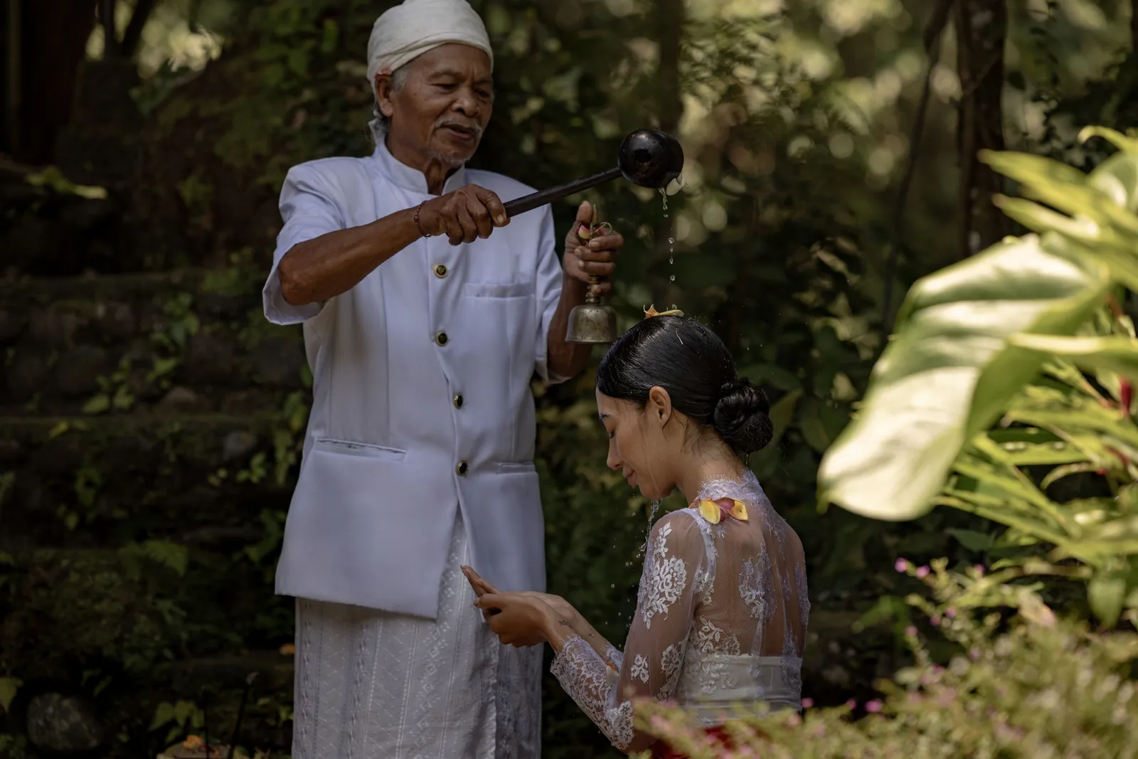 A Balinese priest in white blesses a guest during Melukat, the water rite