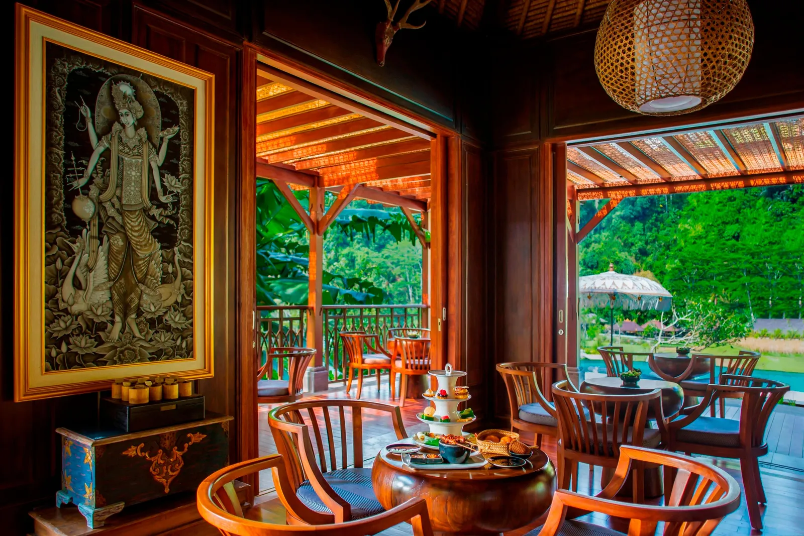 A timber room open to the garden, a Balinese painting on the wall and tea laid out