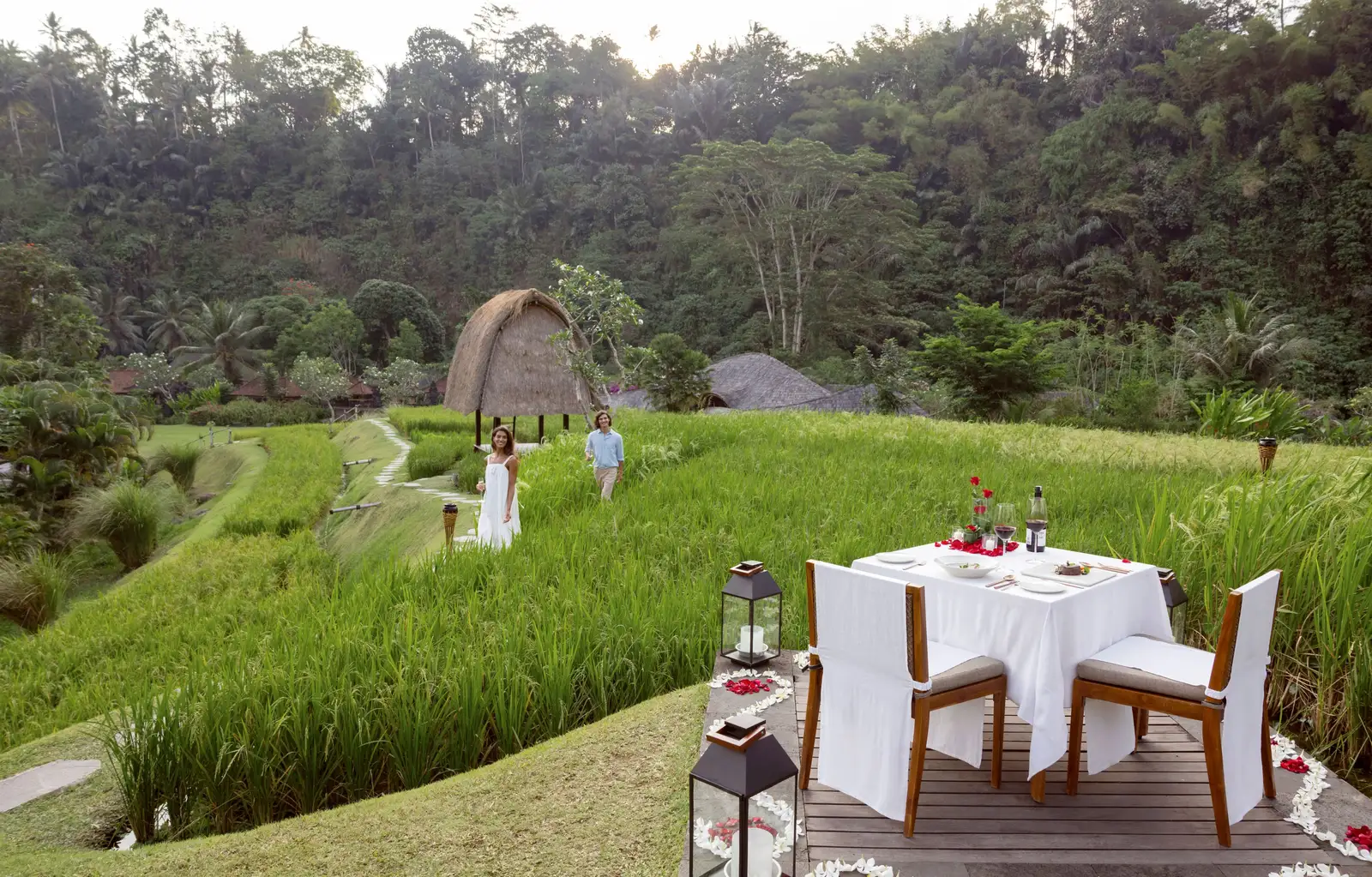 A dinner table laid on the rice terrace, with lanterns and a thatched barn