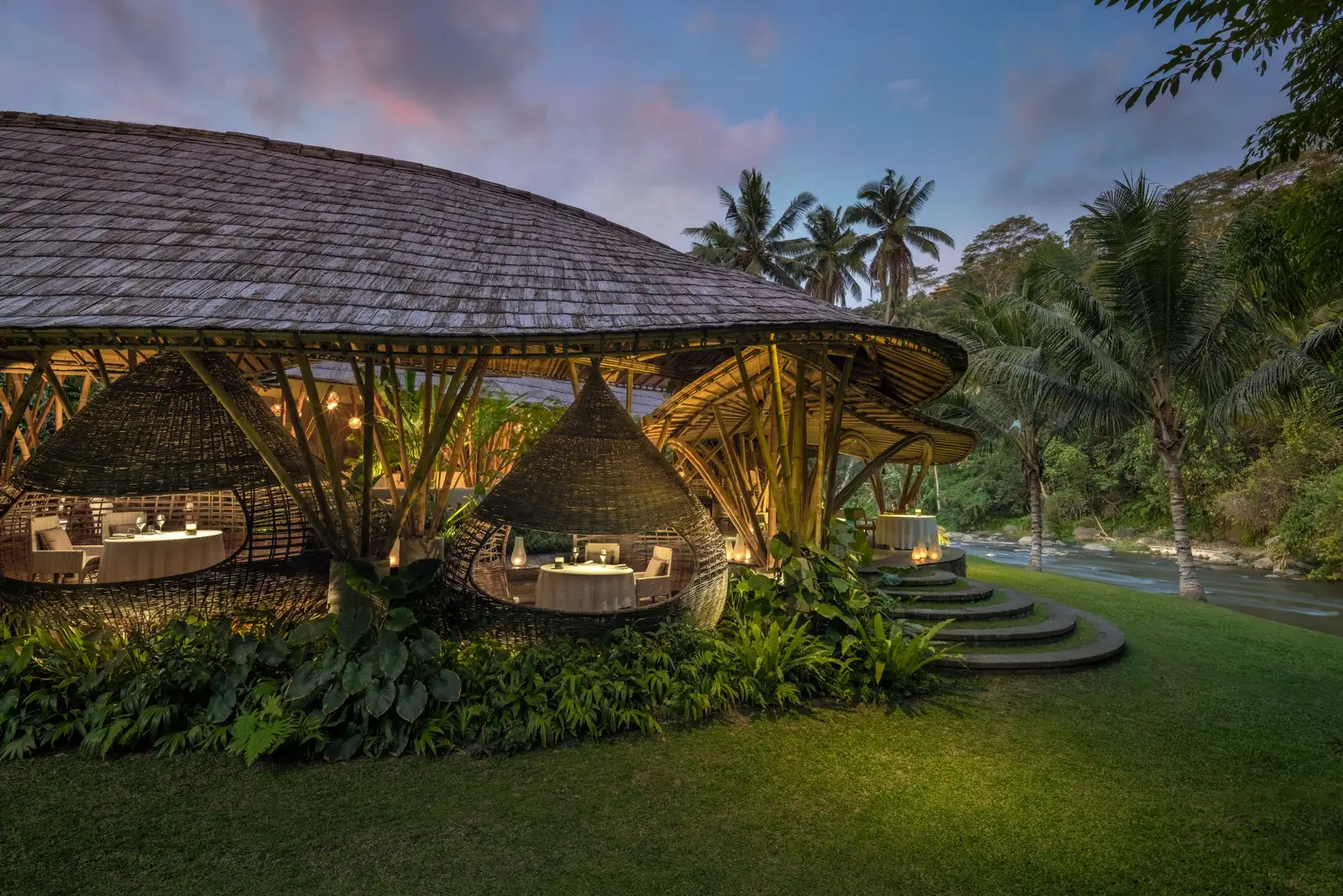 Kubu at dusk: the restaurant’s bamboo shell on the lawn, its cocoons lit and the jungle behind