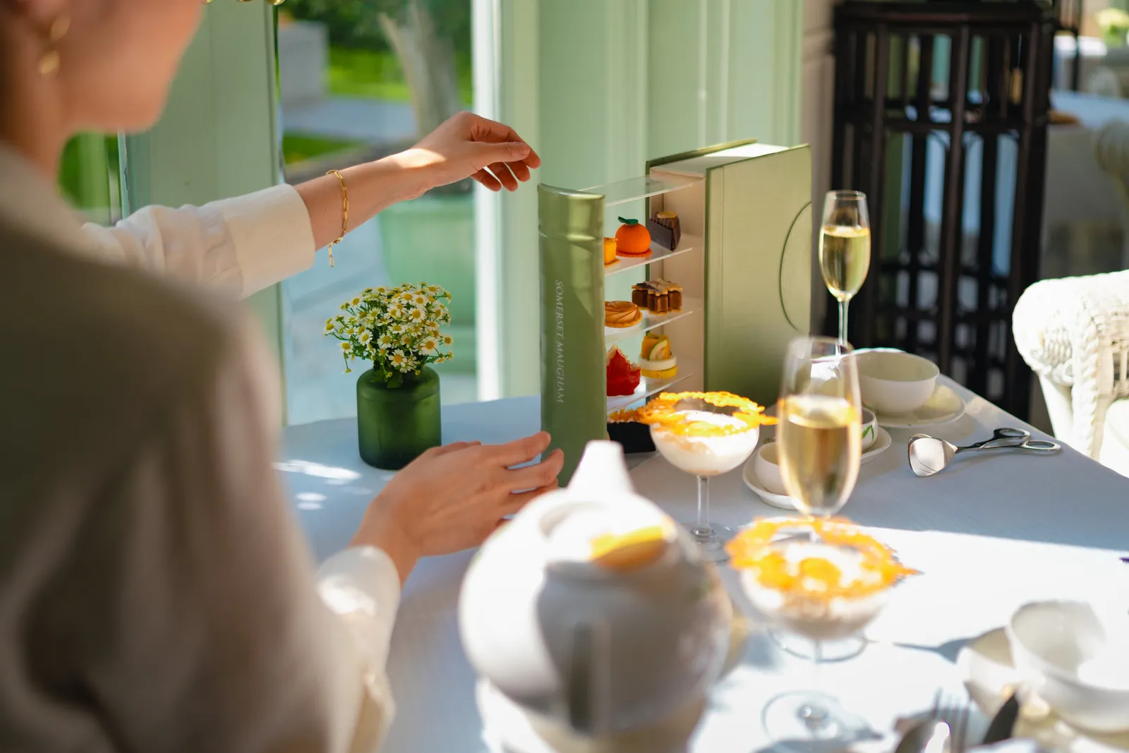 Il tè del pomeriggio nella Authors’ Lounge: l’alzata, un calice di Champagne e una mano che prende un dolce