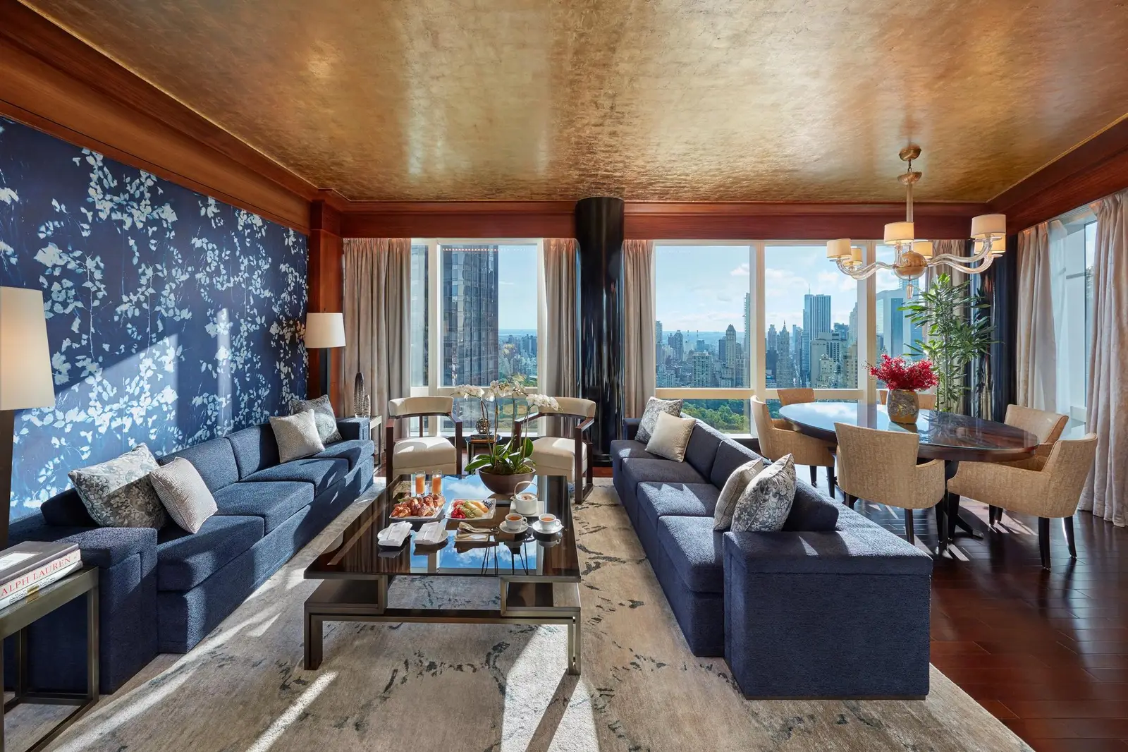Living room with blue sofas, a floral wall and dining table