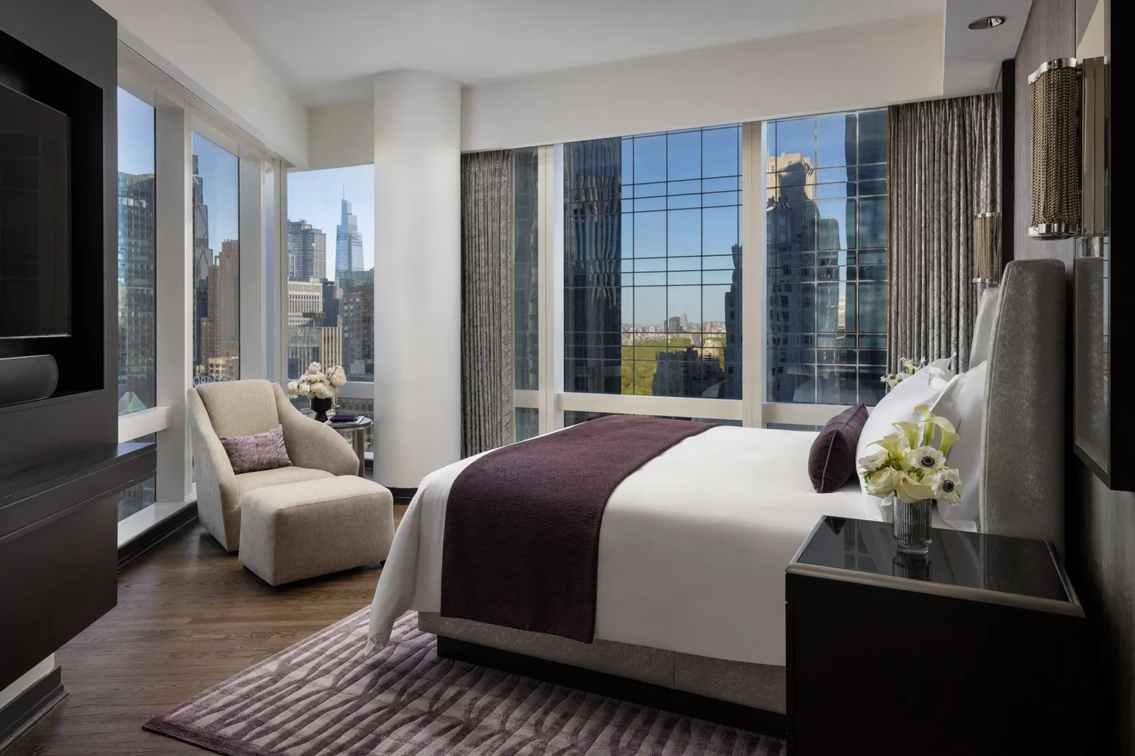 Bed with a purple runner and windows facing the skyscrapers