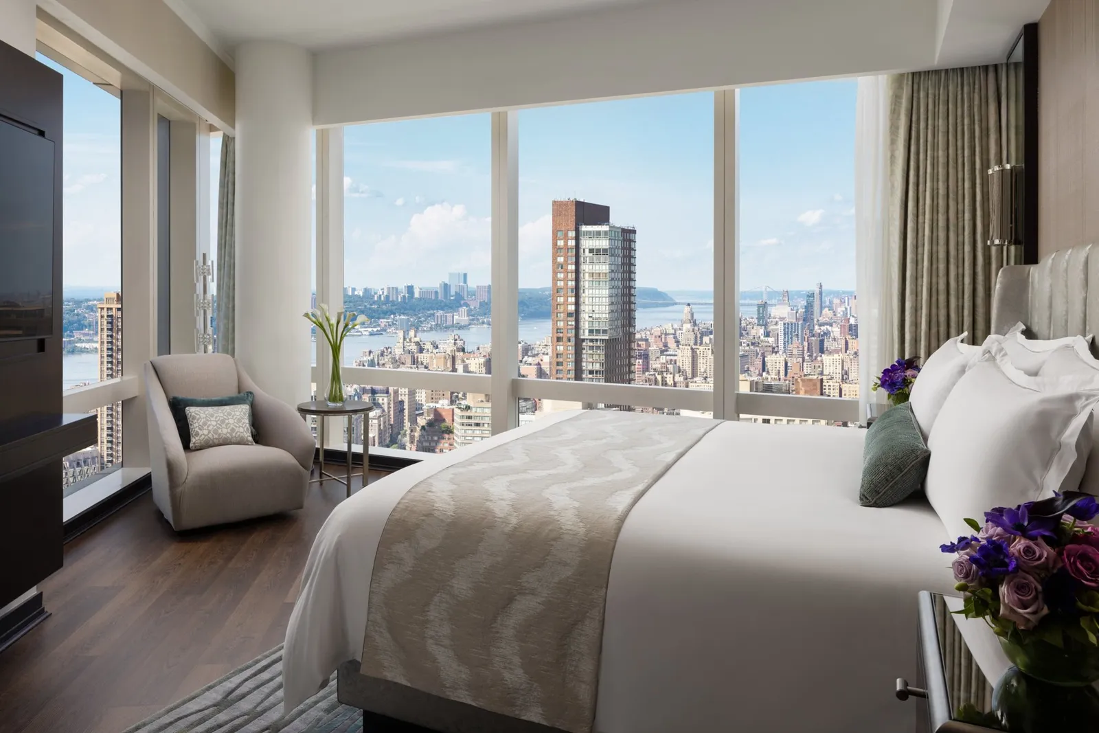 Double bed and armchair between corner windows overlooking the city