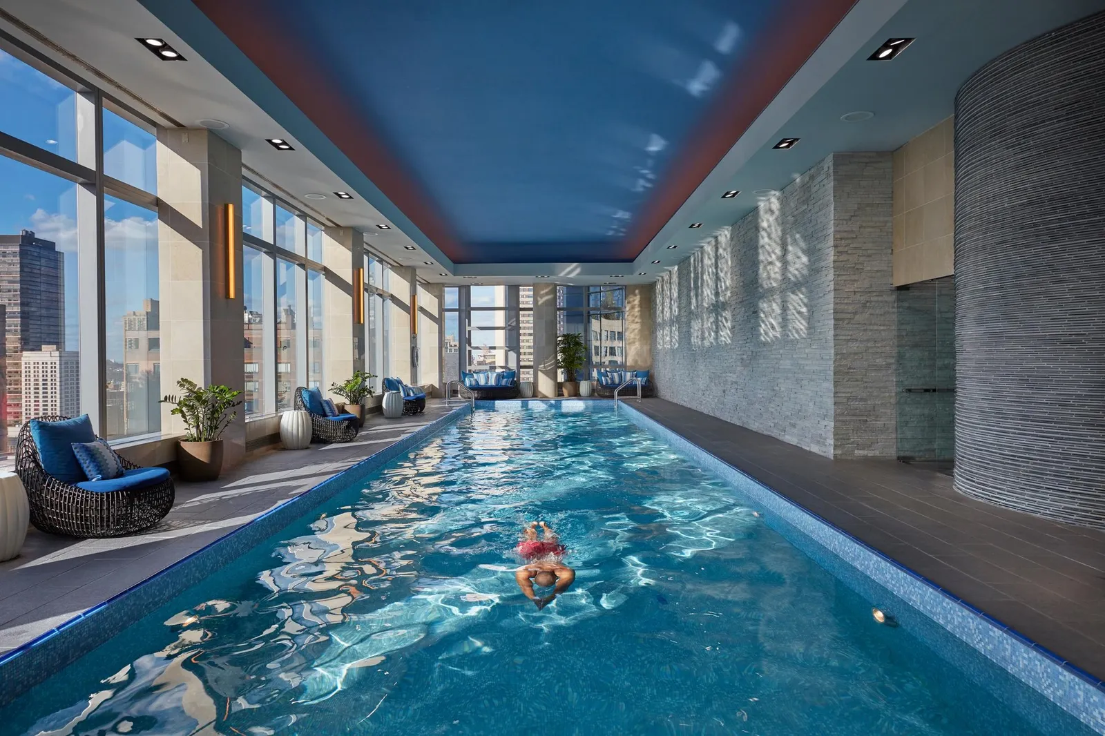 A swimmer in the indoor pool, with loungers and tall windows