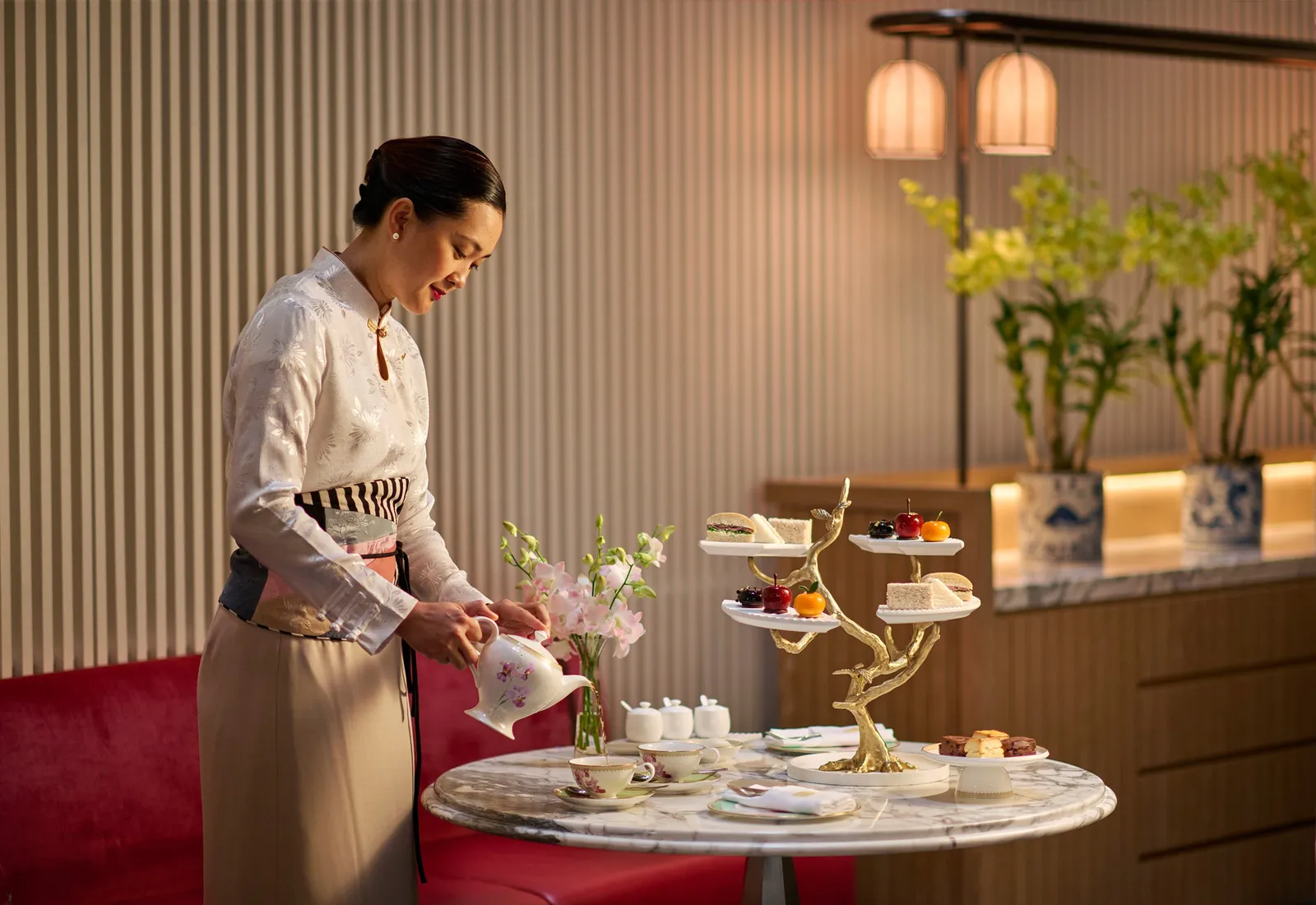 Afternoon tea: a waitress pours tea beside a gilded, branch-shaped stand of cakes and sandwiches.