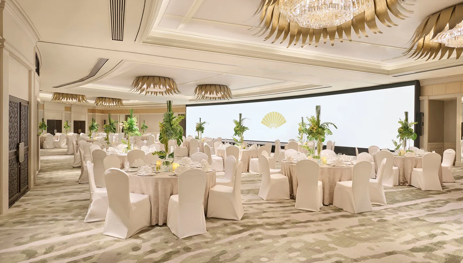 The Oriental Ballroom laid with round tables, white-covered chairs, chandeliers of gilded leaves and a large screen.