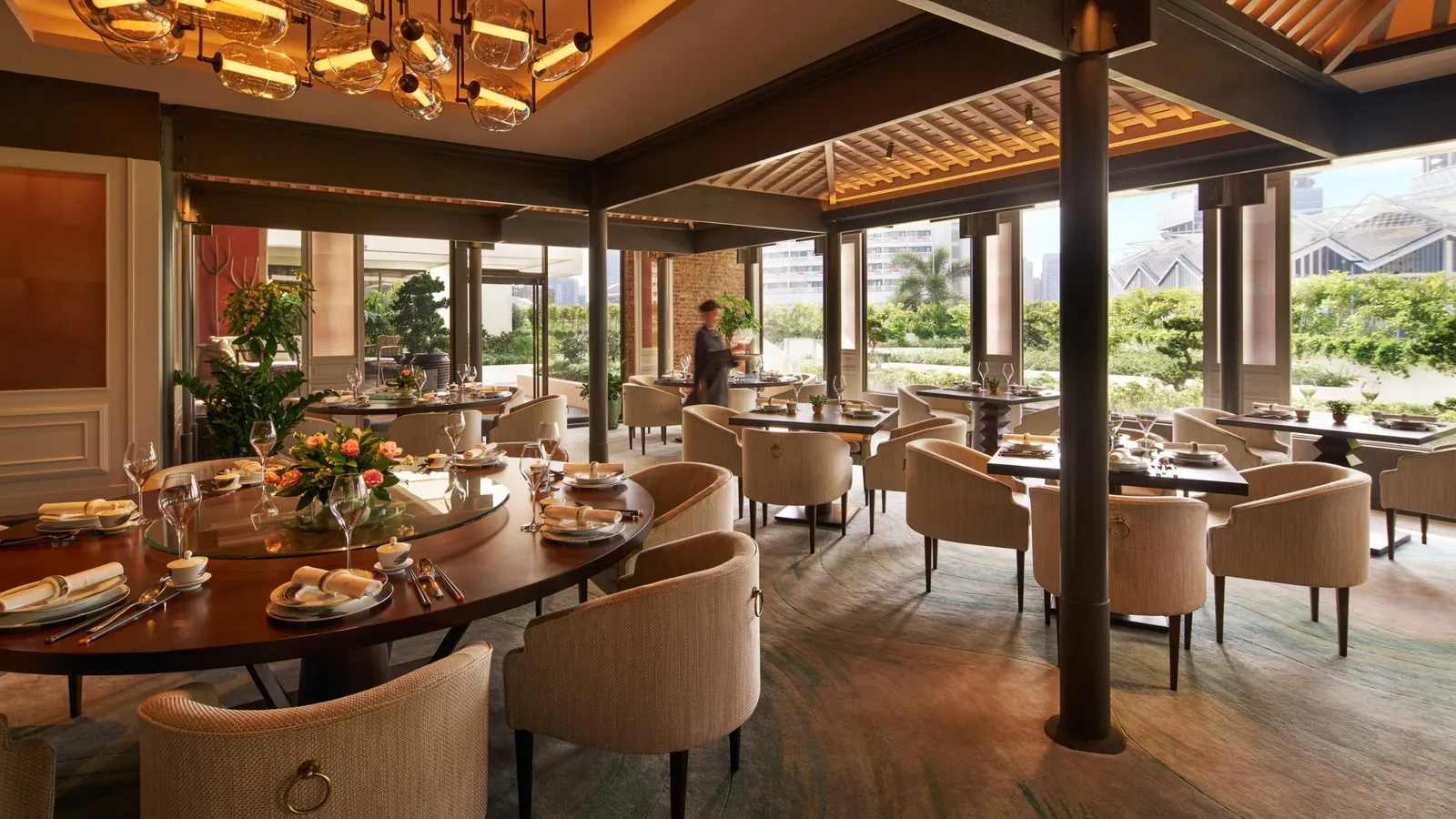 Cherry Garden: a round table laid with a lazy Susan, pale armchairs, timber beams and windows onto the garden.