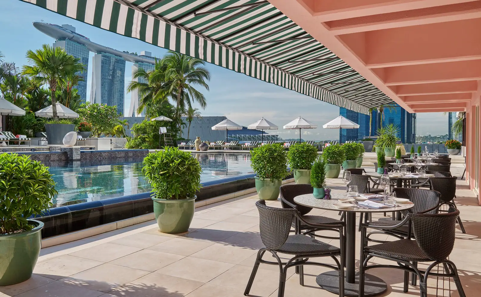 Dolce Vita’s outdoor tables under the striped awning beside the pool, with Marina Bay Sands’ 3 towers in the background.