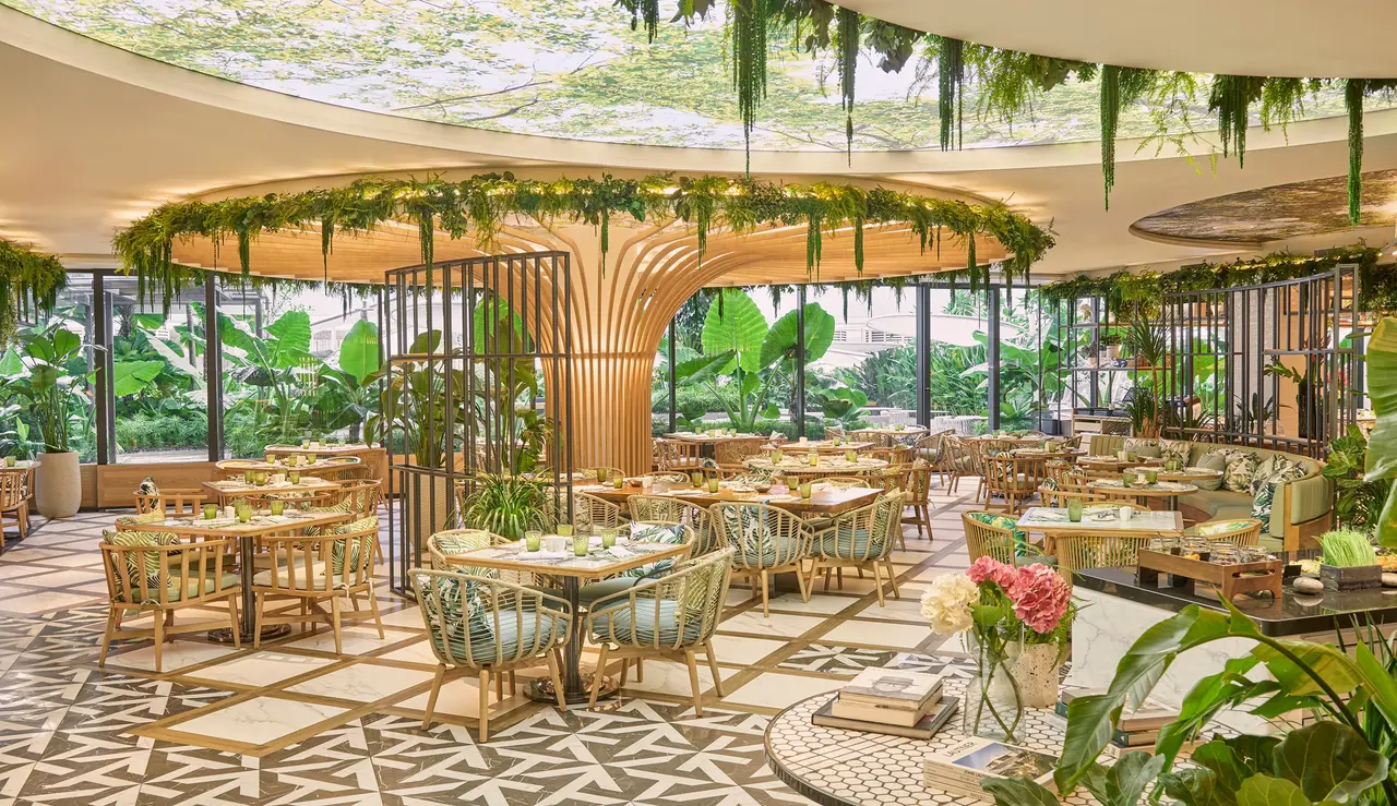 embu’s dining room: rattan chairs and tables round a tree-shaped column, with foliage hanging from the ceiling and a triangle-patterned floor.