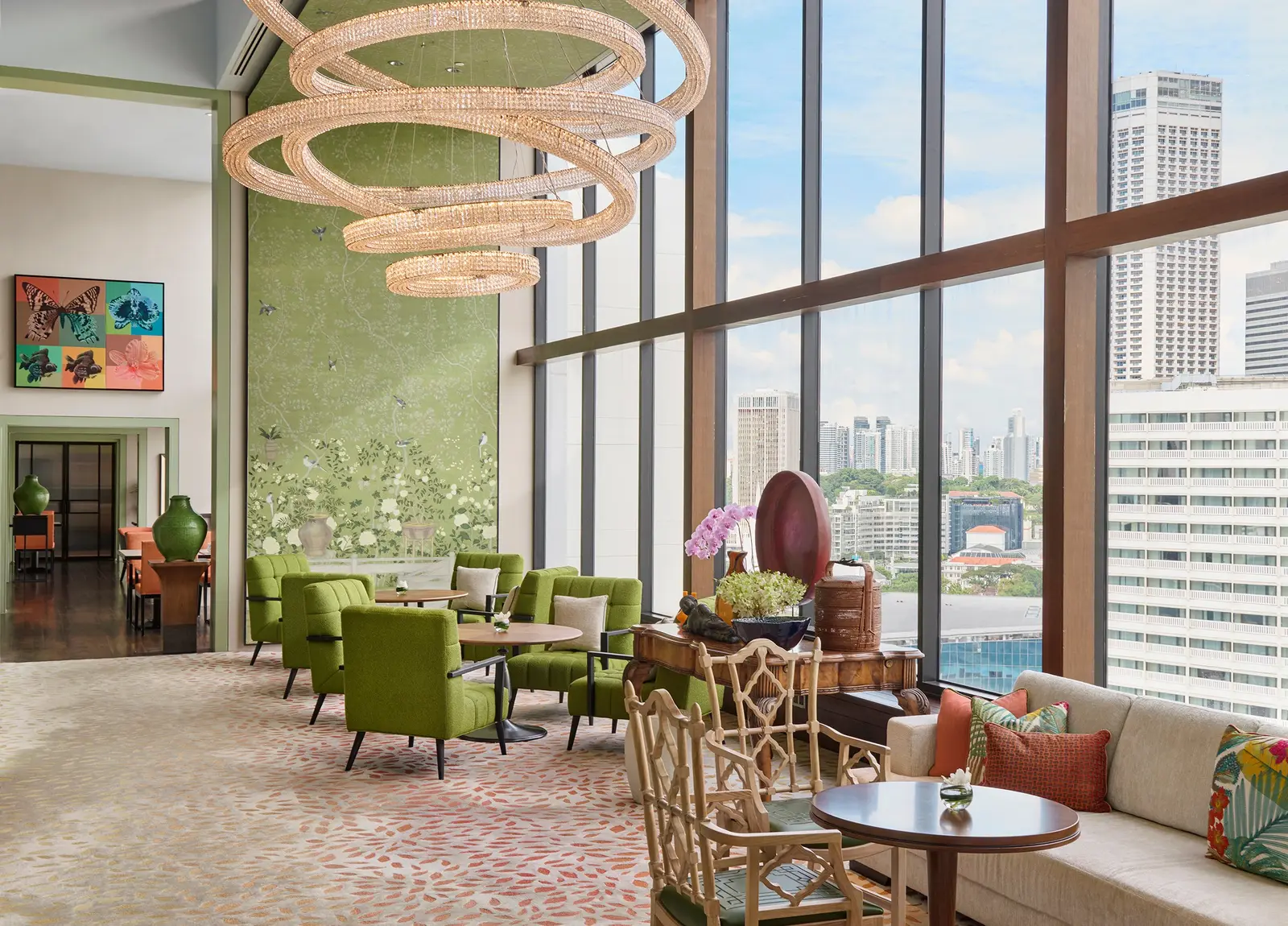 HAUS 65: green armchairs and small tables by full-height windows, a wall painted with flowers and birds and a chandelier of crystal rings.