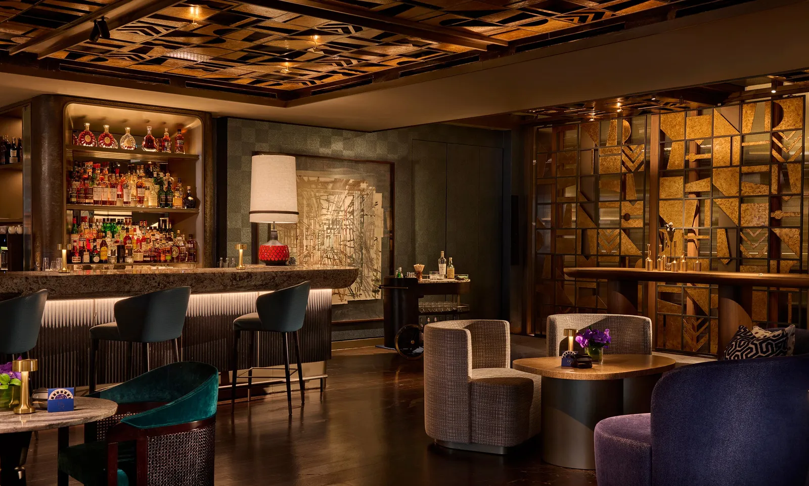 Inside MO BAR: the lit counter with bottles behind it, dark green stools and a ceiling of carved wooden panels.