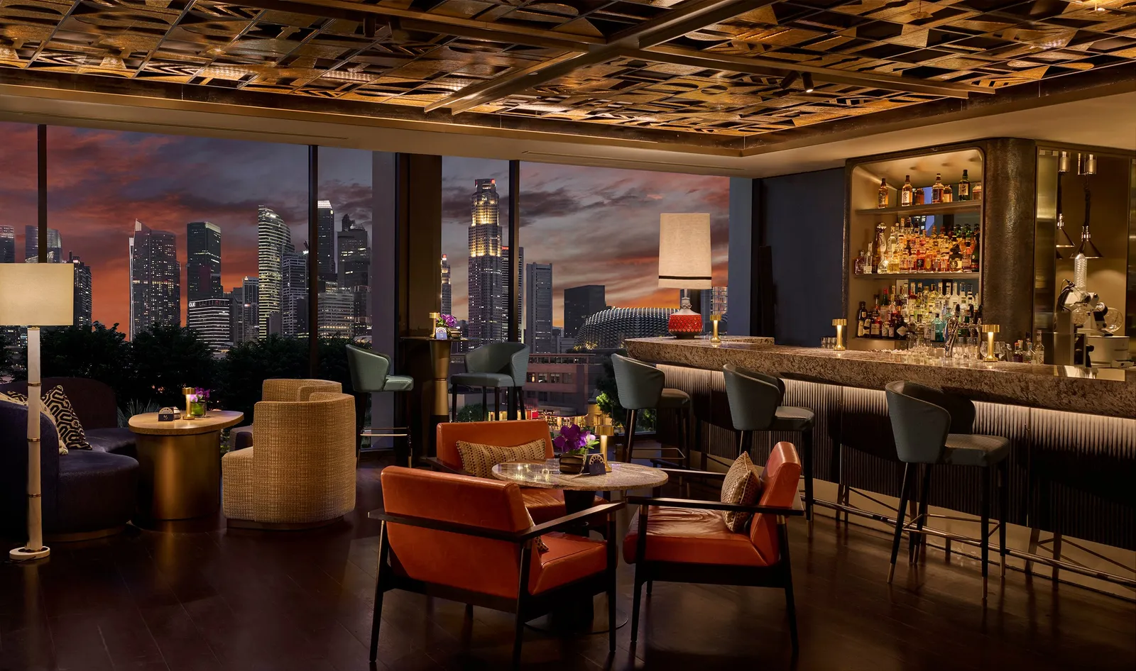 MO BAR at sunset: the stone counter with its stools, orange armchairs and, through the windows, the towers lighting up.