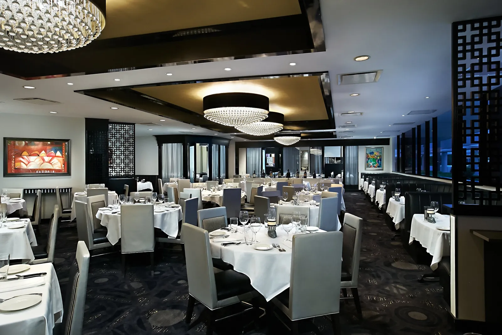 The dining room of Morton’s, The Steakhouse: white-clothed tables, grey chairs and round chandeliers.