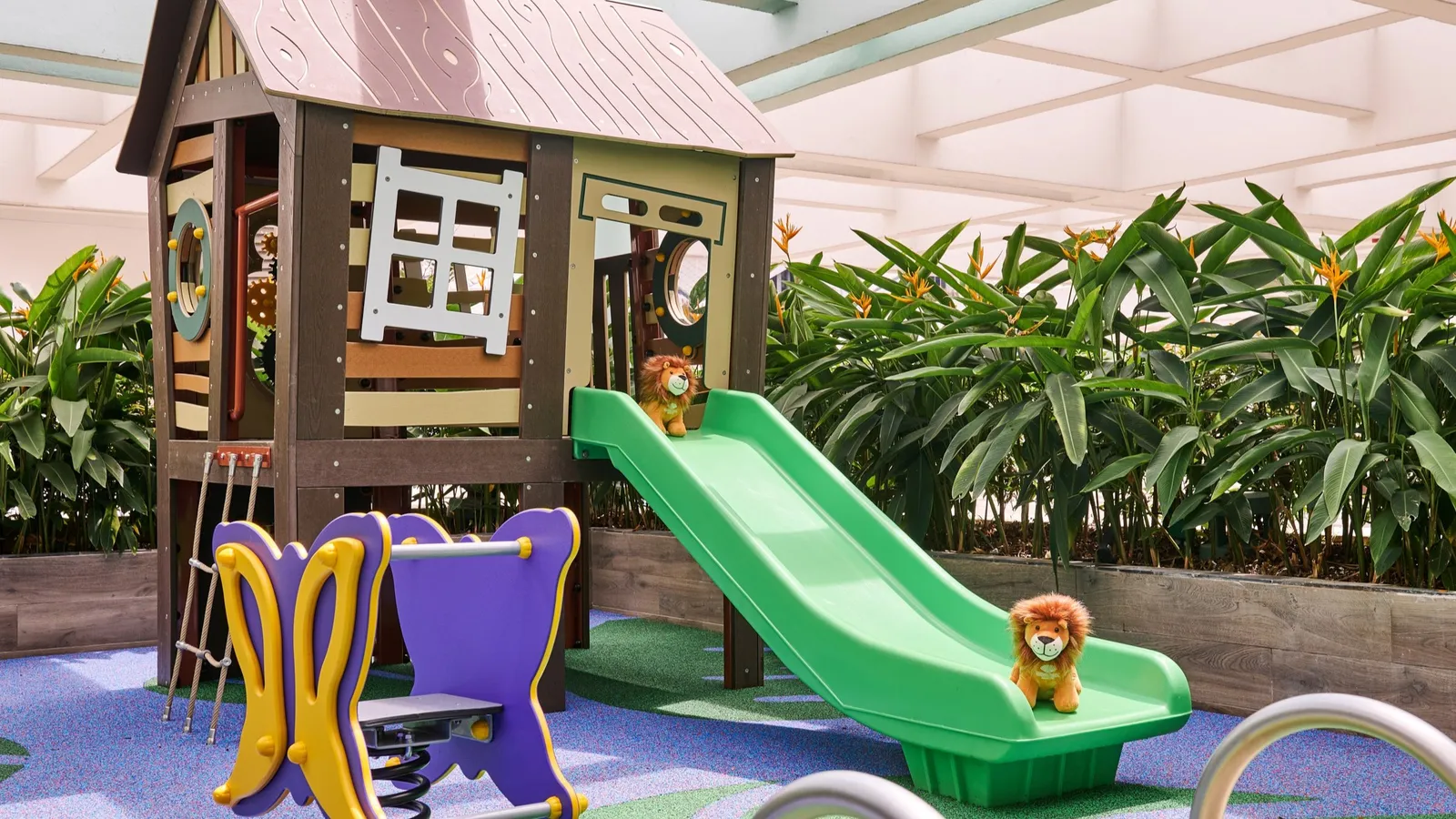 embu’s outdoor playground: a wooden playhouse with a green slide, a rocker and a toy lion.