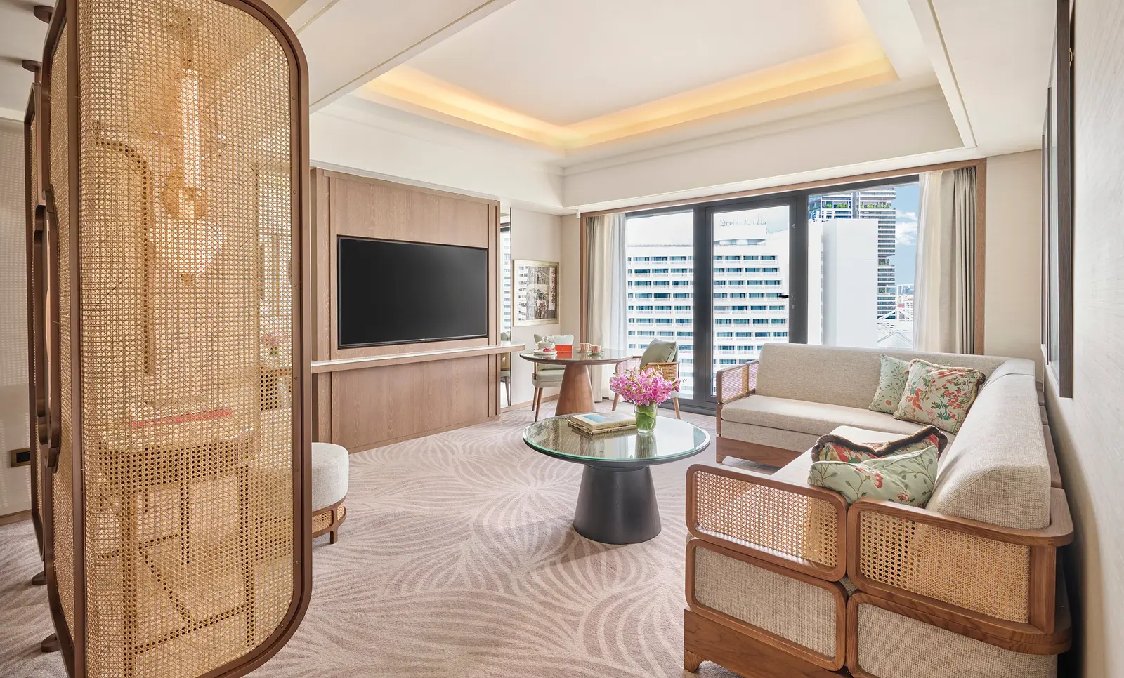 A suite’s living room with a rattan sofa, a round coffee table, the TV and a cane screen, as the Family Suite’s page shows it.