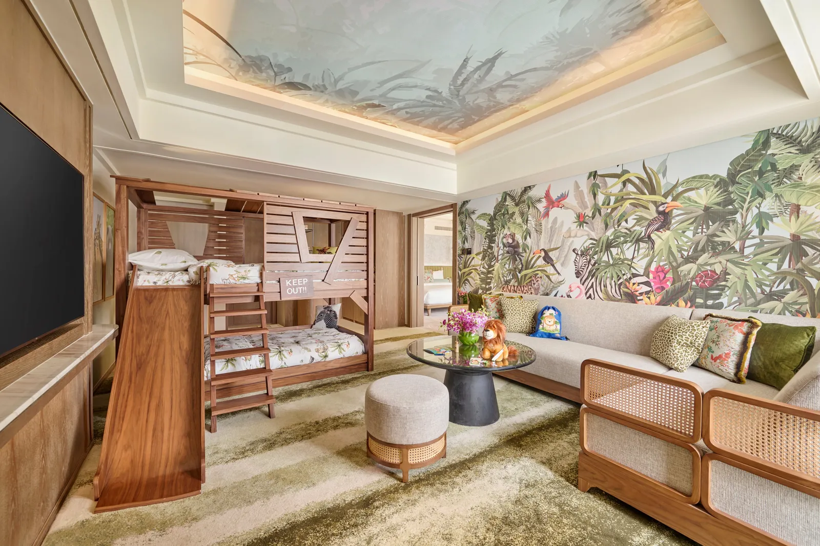 The safari-themed Family Theme Suite: a wooden bunk bed with a slide, the sofa and a wall painted with jungle animals.