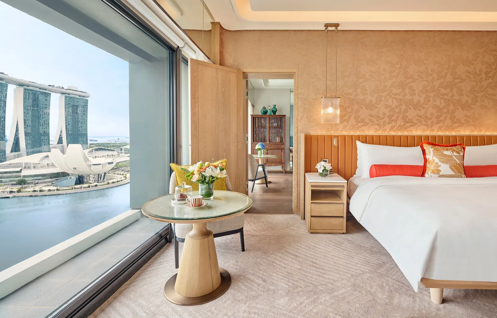 A connecting bedroom of the Royal Marina Bay Penthouse: the bed with orange cushions and, in the window, Marina Bay Sands and the ArtScience Museum.