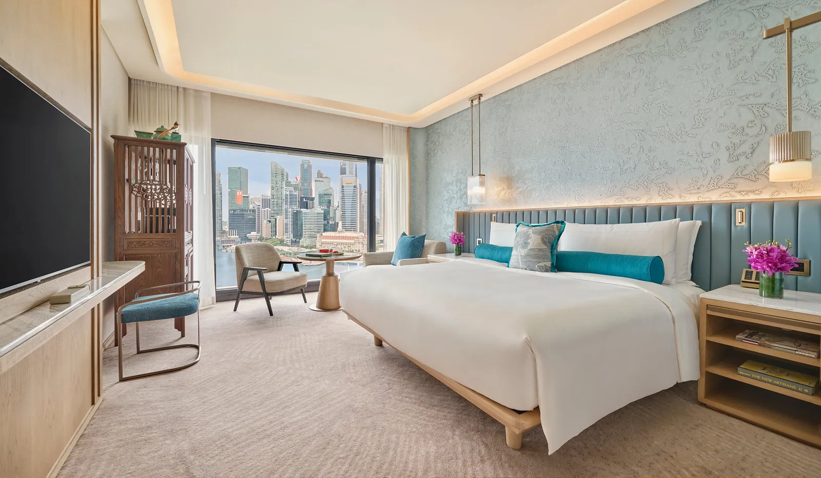 The Marina Bay View Room: the bed with its blue headboard, an armchair by the window and the towers across the bay.