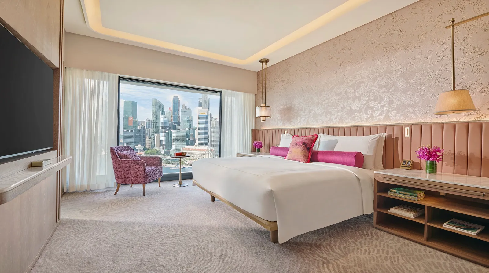 The bedroom of the Premier Marina Bay Suite: the bed with its pink headboard, a purple armchair and the bay in the window.