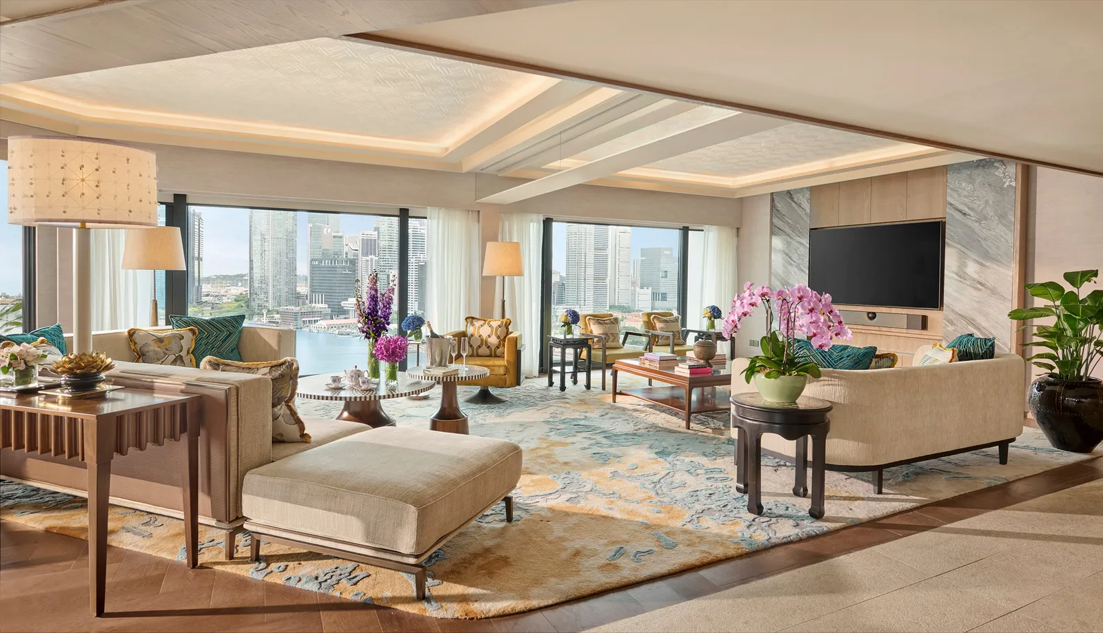 The living room of the Royal Marina Bay Penthouse: pale sofas, a blue and gold rug and windows onto the bay.