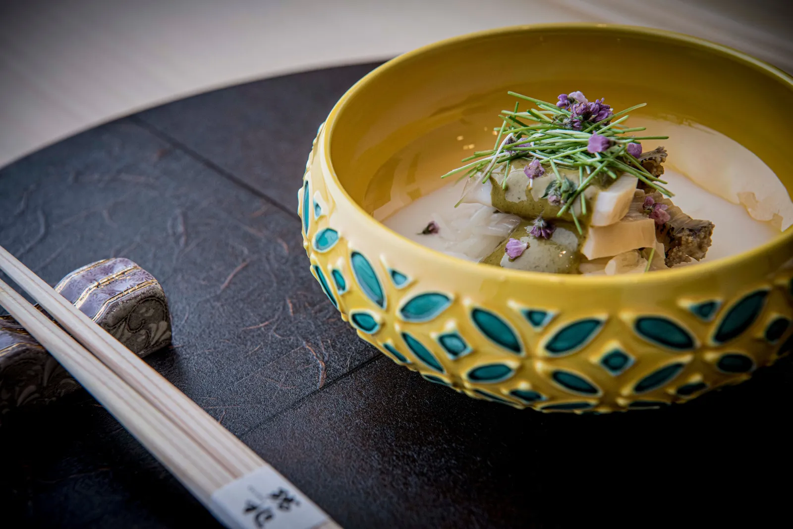 A dish at Zuicho in a yellow and turquoise bowl, with chopsticks laid beside it.