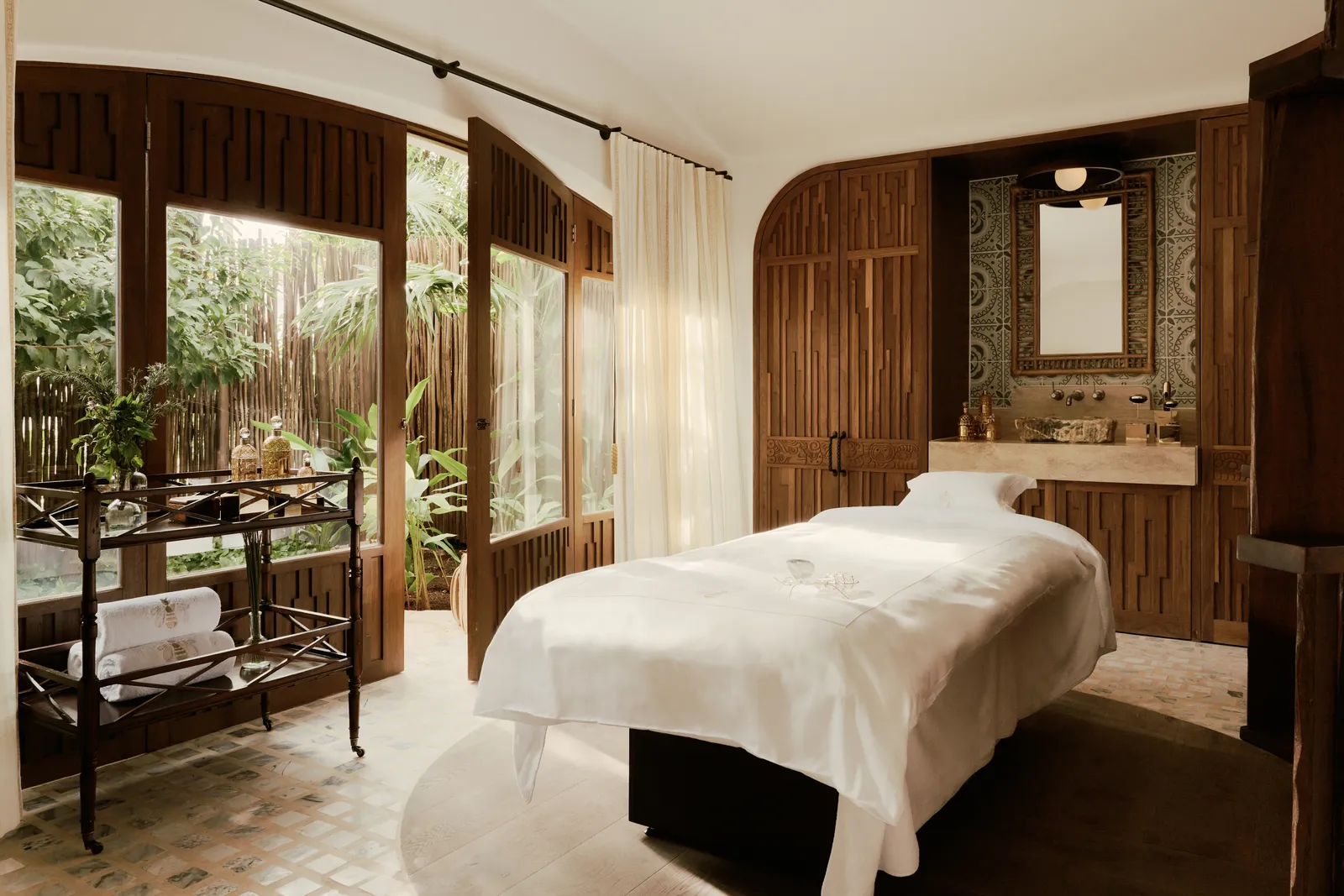 La cabina di Guerlain: un lettino bianco davanti alle finestre sul giardino, pareti di legno e lavabo di marmo