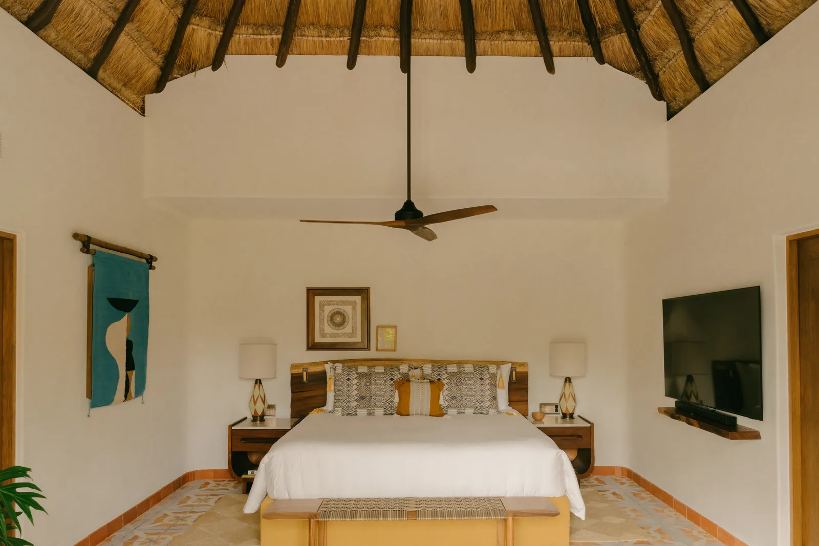 Un letto della Two Bedroom Suite sotto il soffitto di paglia, con tessuti bianchi e gialli