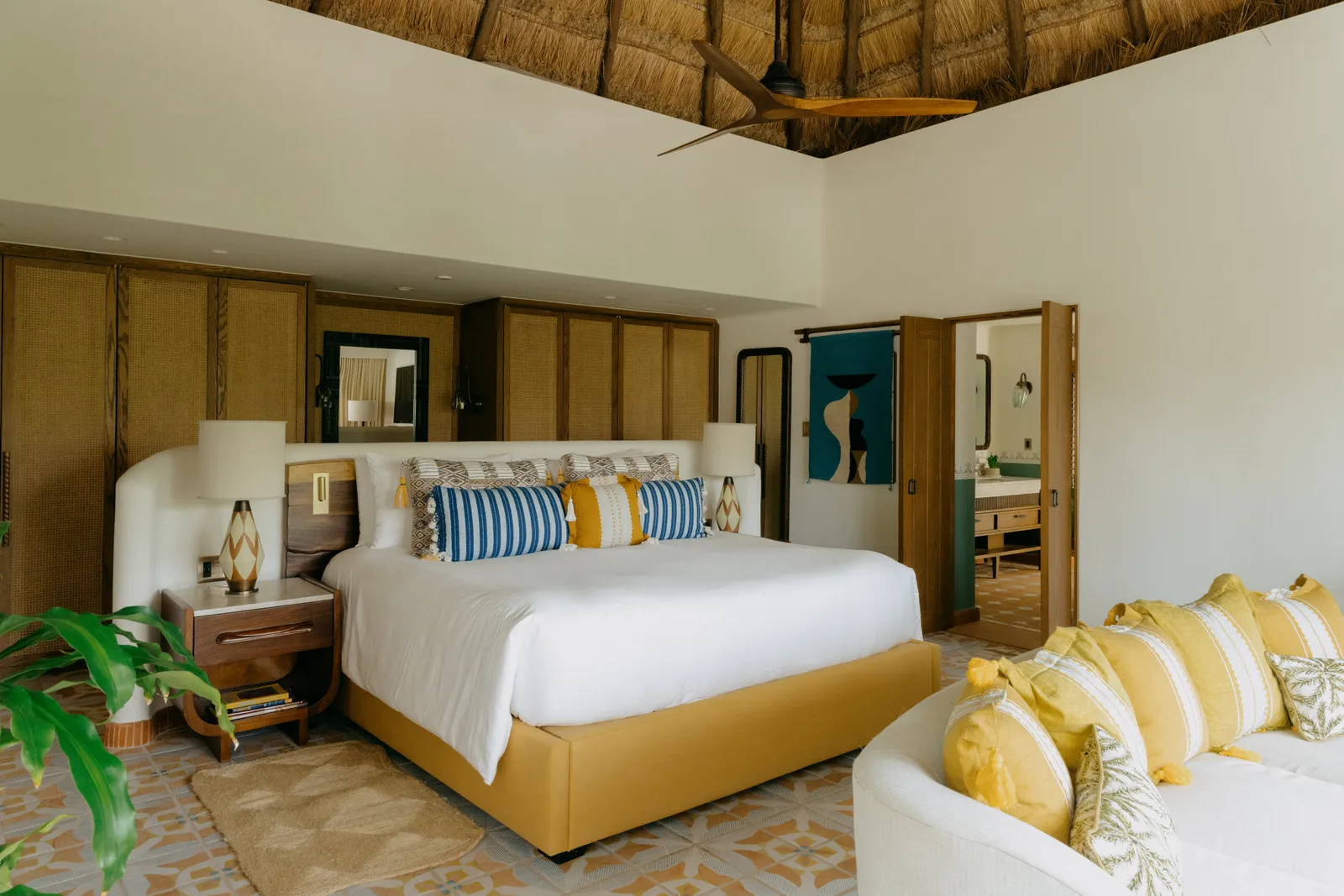 Il letto della Wellness Suite sotto il soffitto alto di legno, con un divano chiaro ai piedi