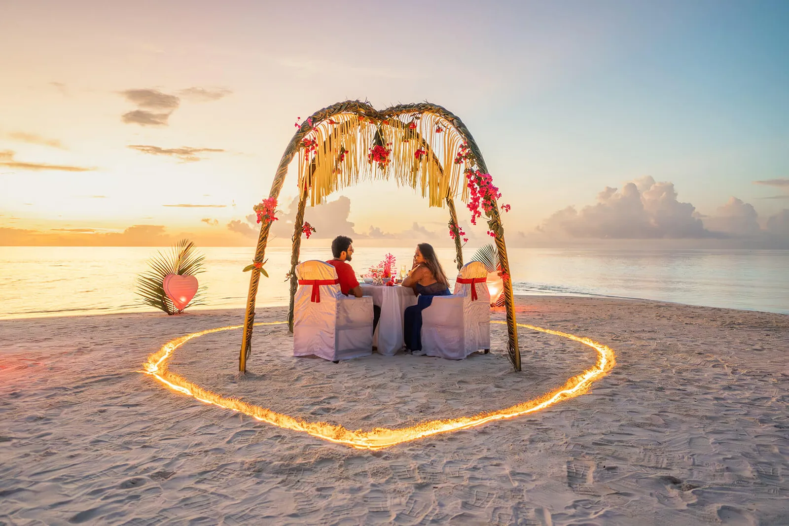 Dinner for 2 on the beach at sunset, under an arch of flowers, inside a heart of lights in the sand.