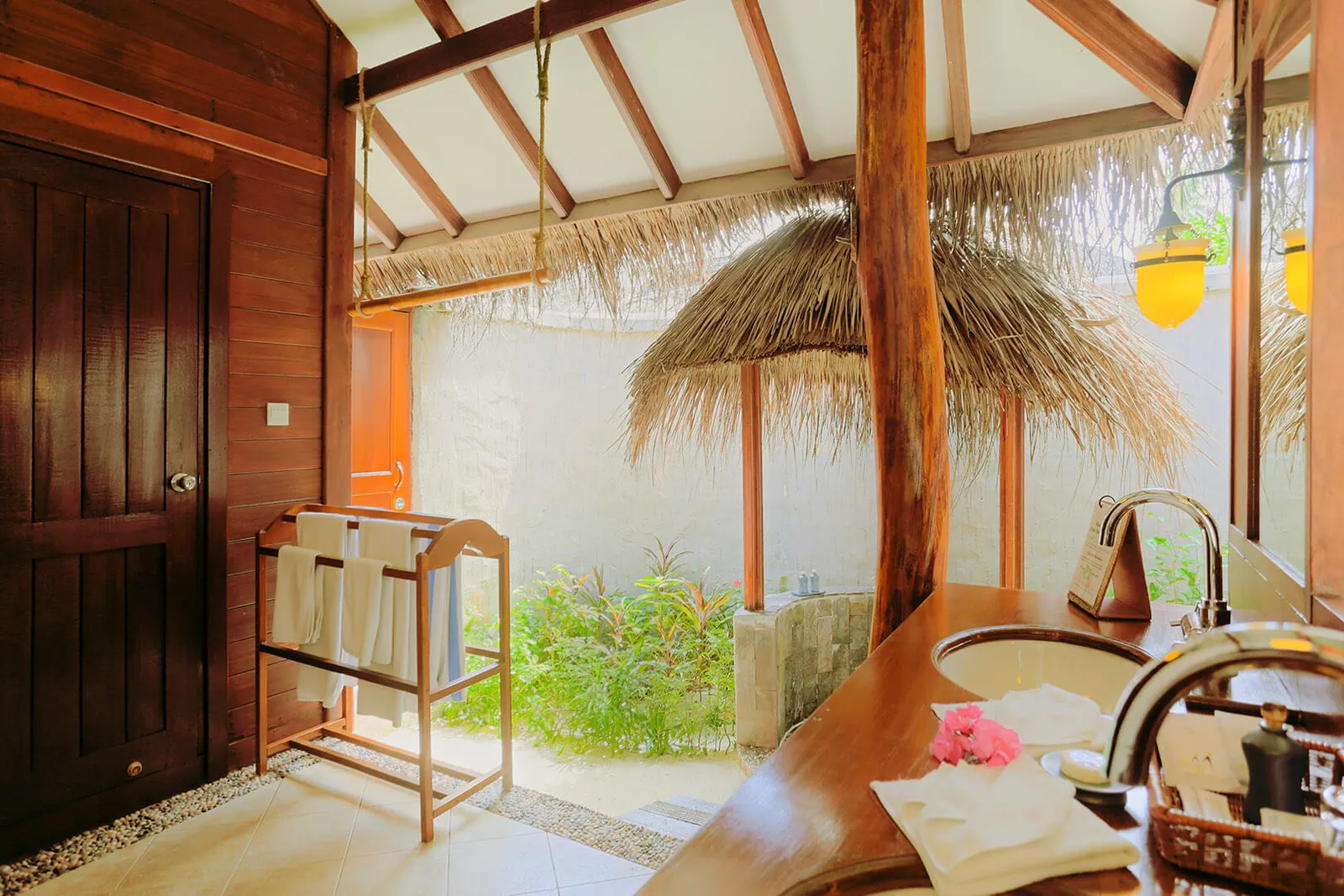 A beach villa’s open-air bathroom: the timber vanity, the towel rail and the shower under a thatched parasol.