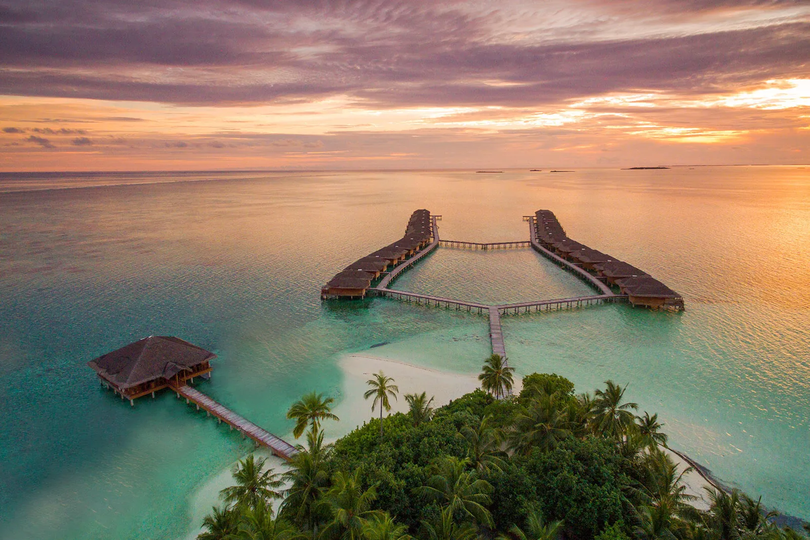 The 2 rows of water villas at sunset, seen from above the island’s palms, with a lone pavilion out in the lagoon.