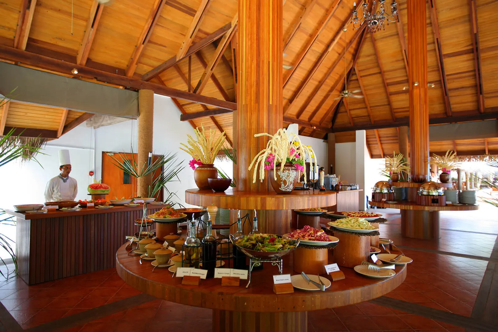 The Malaafaiy buffet: a round counter of dishes around a timber column under the pitched roof, with a chef behind.