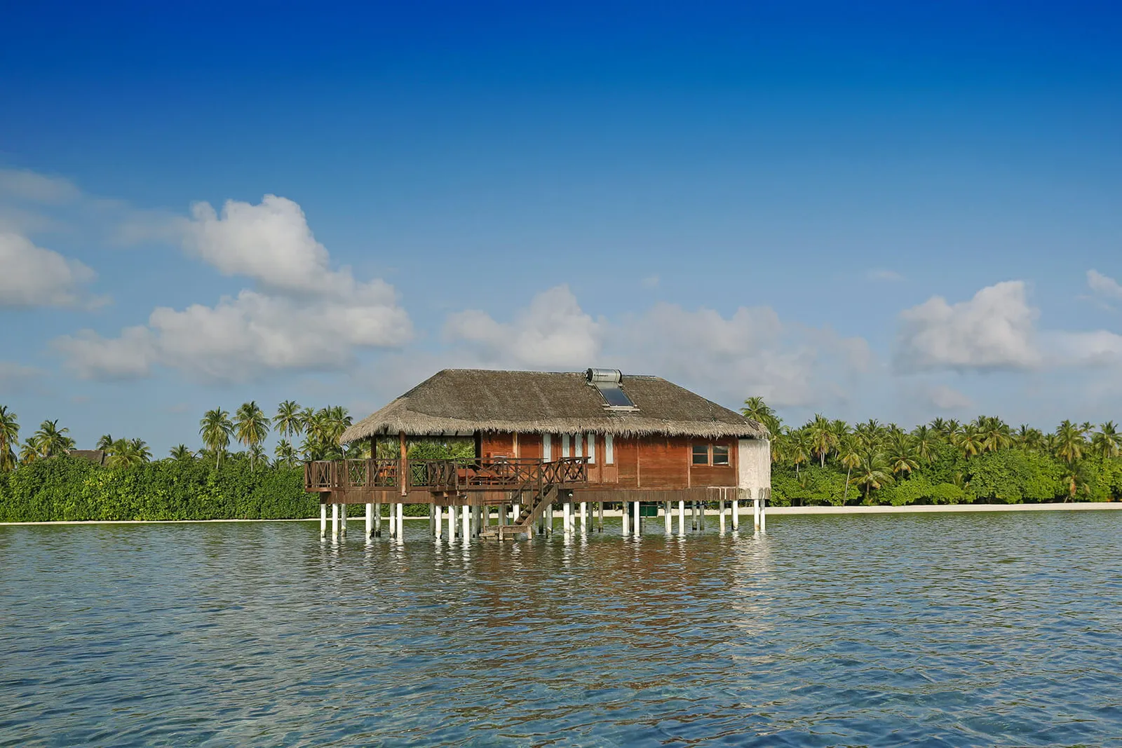 One of the 2 lagoon suites, on stilts with a thatched roof, standing alone off the island’s green shore.